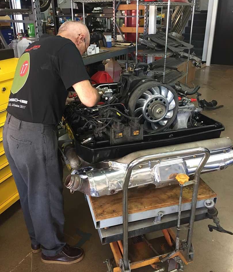 A Porsche flat-six engine out of the car on a bench trolley, exhaust system alongside.