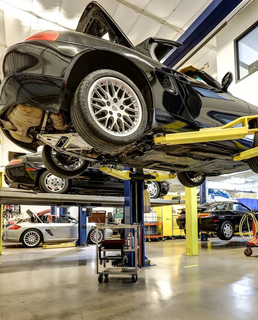 A Porsche raised on a two-post lift with its underside, exhaust and suspension exposed for inspection.